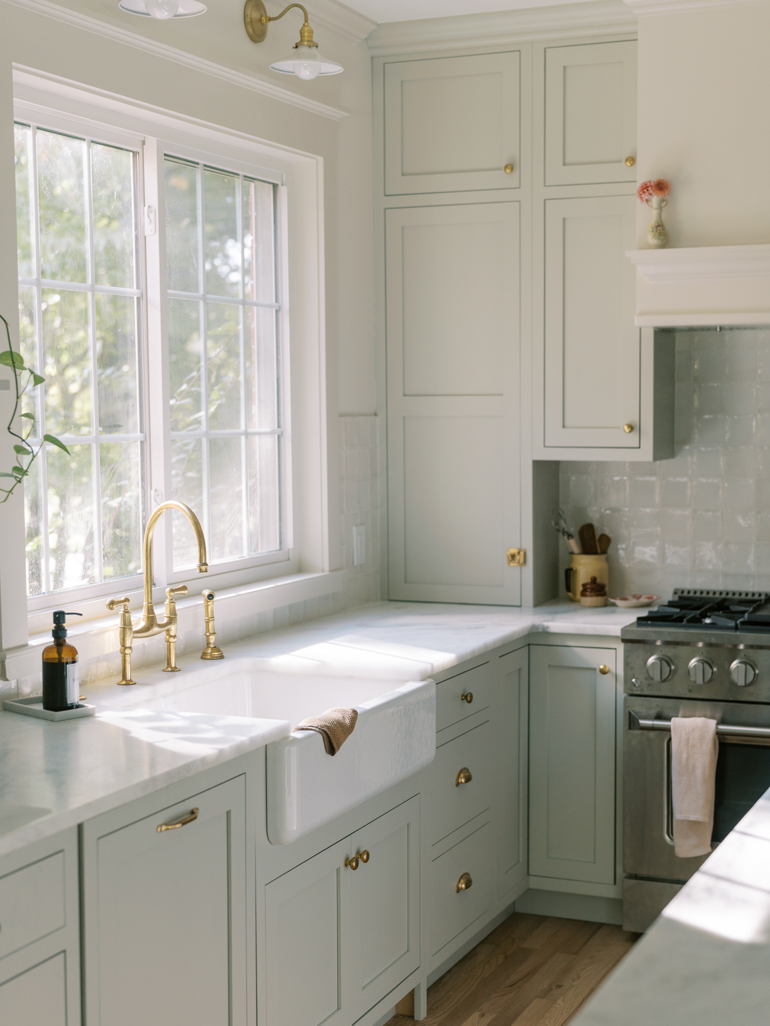 Stunning kitchen with remodel with the Cabinet Joint using creamy paint colors, soft green cabinets, brass faucet, and kohler whitehaven farmhouse sink.