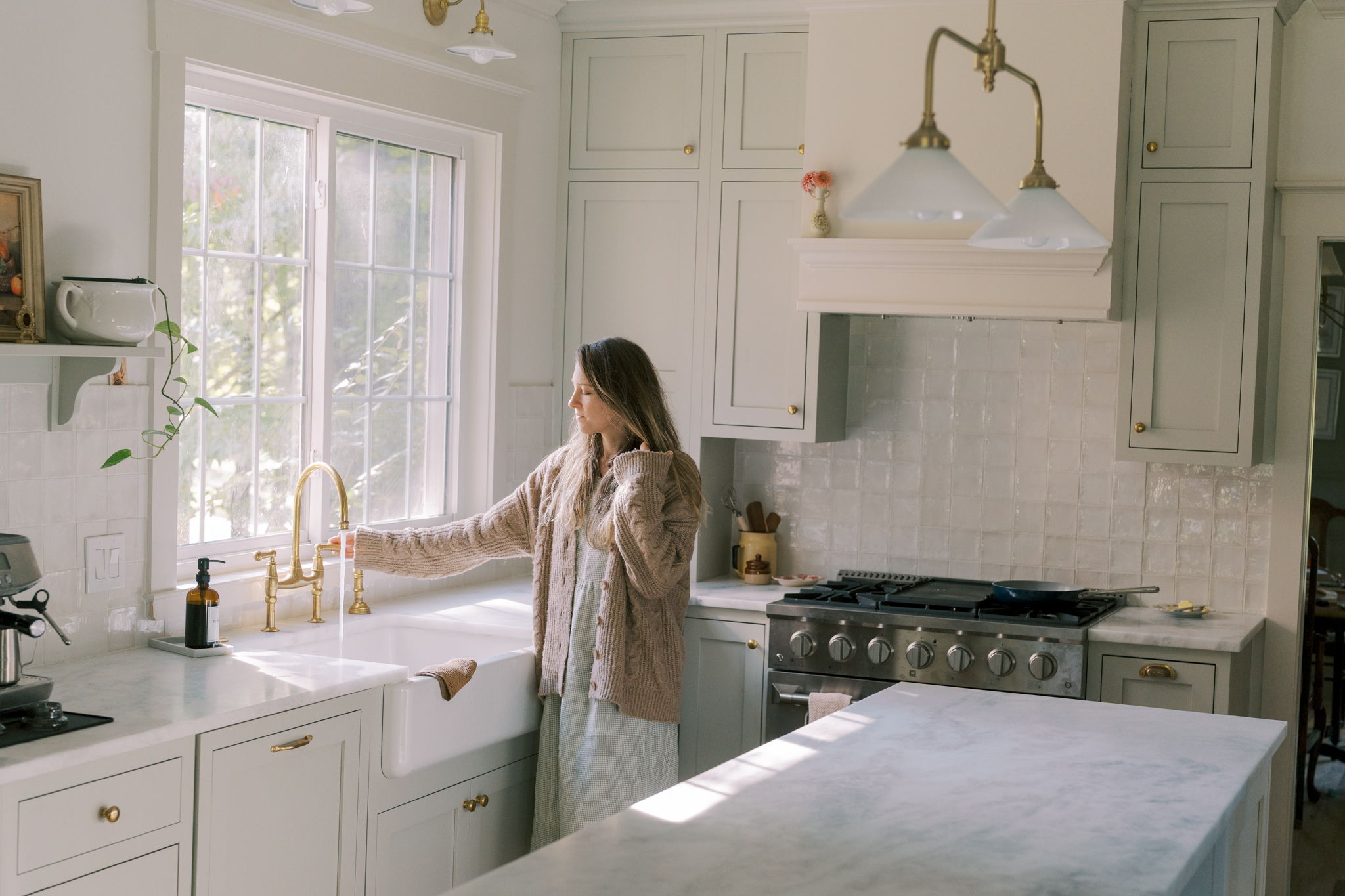 Woman in a beautiful kitchen with natural light and creamy warm paint colors using the Perrin and Rowe Unlacquered Brass Faucet.