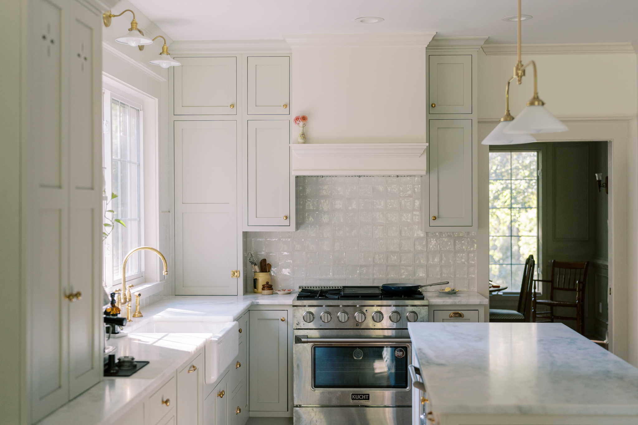 Kitchen with creamy tones, inset cabinets, handmade tiles, kucht oven, marble counters, and brass details.