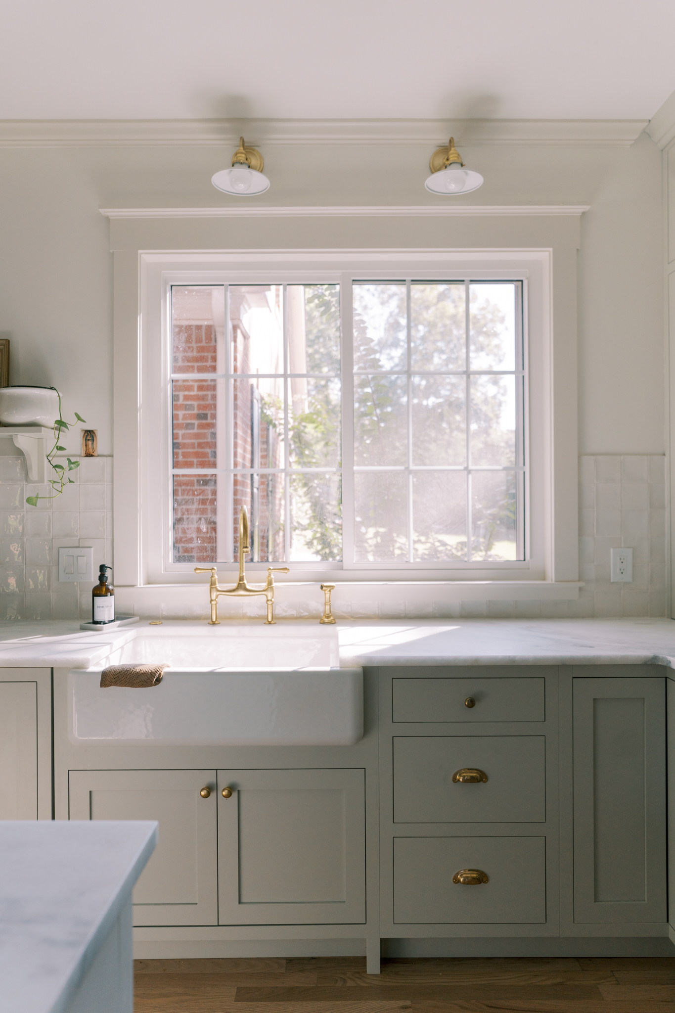 Kohler Whitehaven sink with brass faucet and large kitchen window with natural light. 