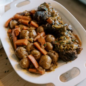 Slow cooker pot roast served on a platter with tender beef, carrots, and baby potatoes in rich gravy.