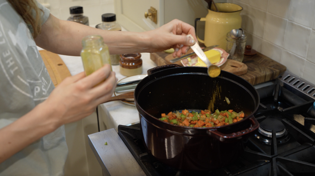 woman cooking veggies in a pot and adding seasonings