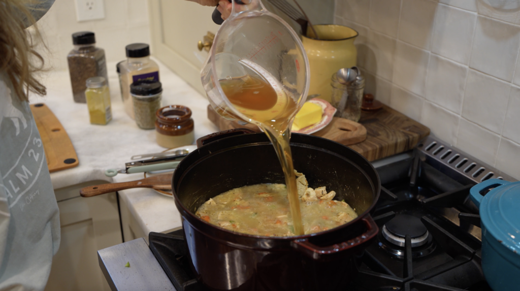 woman adding broth to a pot of soup