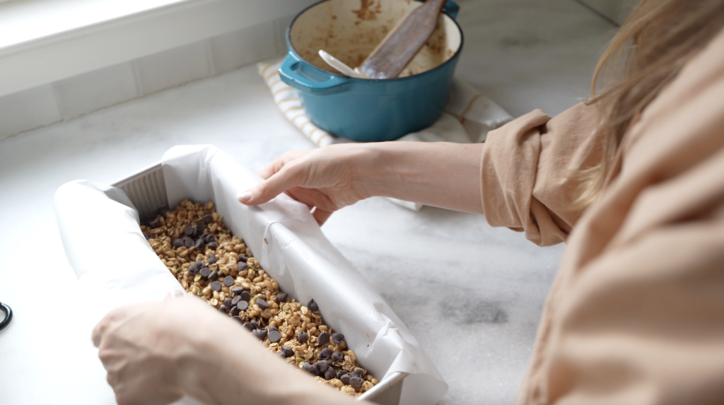 woman making homemade snacks for kids with granola bar mixture in a parchment lined pullman loaf pan 