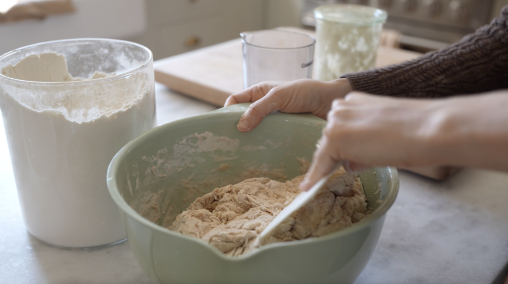 hand mixing up bread dough in a beautiful blue bowl in a naturally lit kitchen 