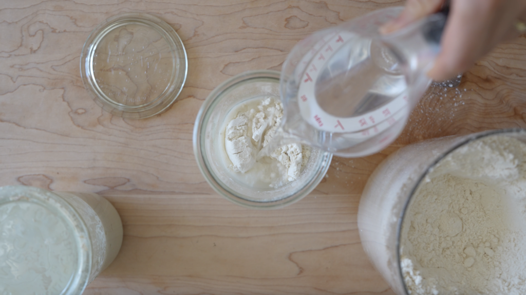 hand pouring water into a weck jar of flour and sourdough starter