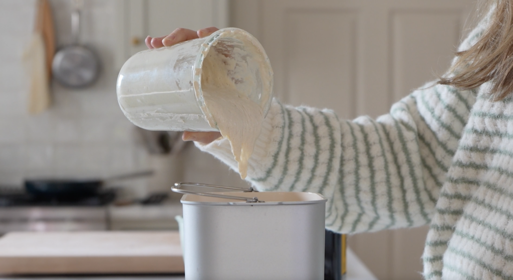 hand pouring sourdough starter into a bread machine bowl