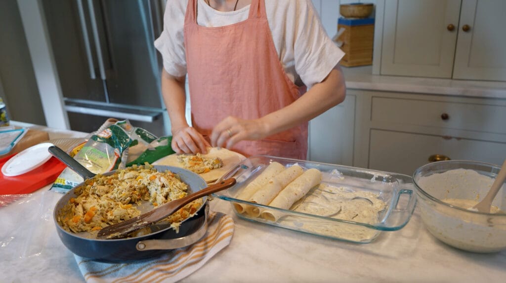 Person filling and rolling tortillas with chicken mixture to assemble enchiladas.