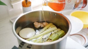 Roasted chicken bones, onions, celery, and garlic being added to an Instant Pot for homemade bone broth.
