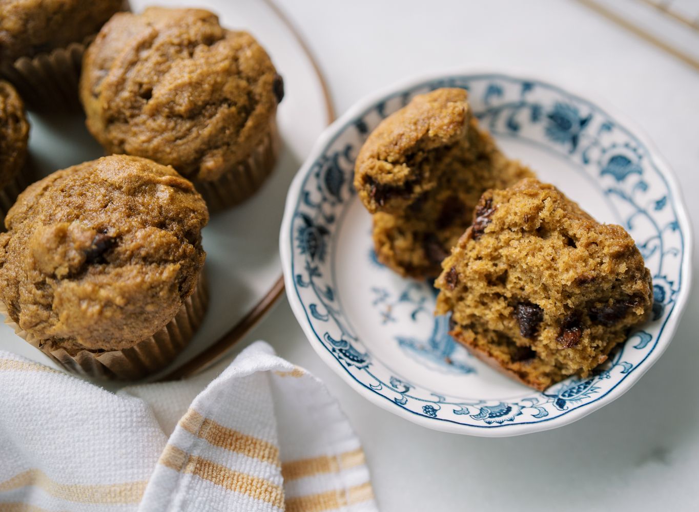 Fresh-milled pumpkin banana muffins with chocolate chips, sliced open to show a moist, fluffy texture on a blue floral plate.
