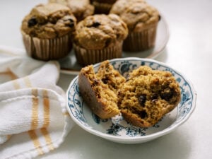 Fresh-milled pumpkin banana muffins with chocolate chips, sliced open to show a moist, fluffy texture on a blue floral plate.