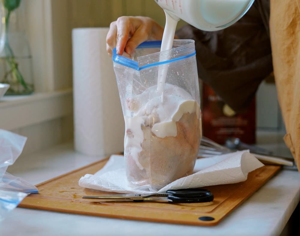 buttermilk being poured into plastic bag to marinate a whole chicken