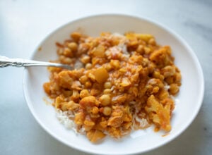 Cauliflower and chickpea stew served over white rice in a white bowl with a spoon