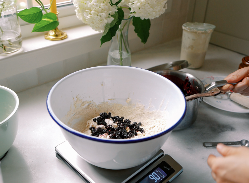 a mixing bowl filled with bagel dough and blueberry compote